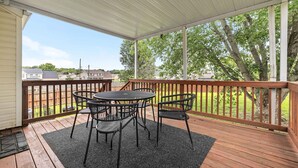 A covered outdoor deck with a table and chairs, a wooden railing, and a view of a residential area with trees and houses. - Cozy Family Retreat Near Fort Campbell, Sleeps 8 (Clarksville)