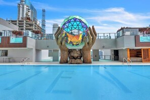 Ein Schwimmbecken mit einer großen, kugelförmigen Skulptur in der Mitte, umgeben von modernen Gebäuden.