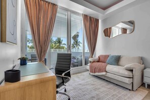 Ein modernes Zimmer mit Schreibtisch, Stuhl, Sofa und großen Fenstern mit Vorhängen.