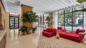 A spacious lobby with a red sofa set, large potted plants, and a view of the street through large windows. - Monthly Stay Studio · Midtown Miami, Free Parking (Miami)