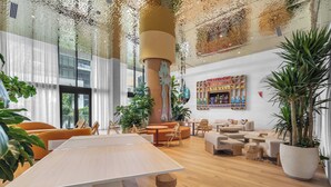 A modern hotel lobby with a large wooden table, comfortable seating, potted plants, and a colorful display of amenities. - Monthly Stay Studio · Midtown Miami, Free Parking (Miami)