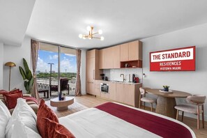 Quarto de hotel moderno com uma cama grande, área de refeições, cozinha e varanda com vista.
