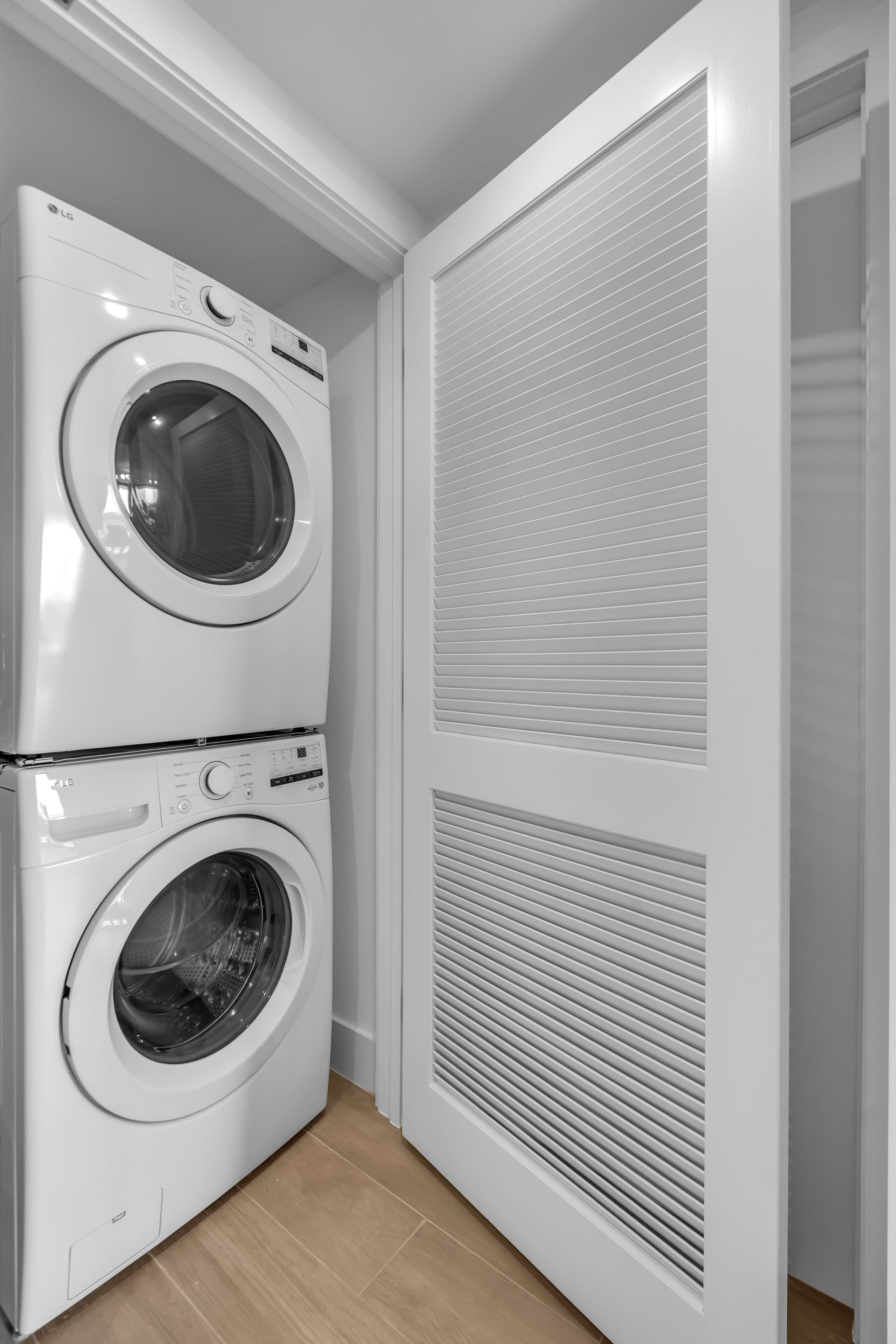 A laundry room with two stacked washing machines and a large louvered door.