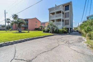 Um edifício com vários andares, varandas, área de estacionamento e um gramado bem cuidado.