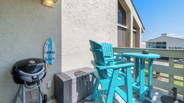 A balcony with a grill, chairs, and a table. - Beachfront Paradise with Stunning Gulf Views (Gulf Shores)