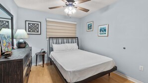 A bedroom with a bed, a ceiling fan, a bedside table, a lamp, and wall art. - Beachfront Paradise with Stunning Gulf Views (Gulf Shores)