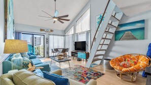 A modern living room with a sofa, a coffee table, a TV, and a staircase. - Beachfront Paradise with Stunning Gulf Views (Gulf Shores)