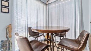 A room with a round table and four chairs, a window with sheer curtains, and a wall with framed artwork. - Beachfront Paradise with Stunning Gulf Views (Gulf Shores)