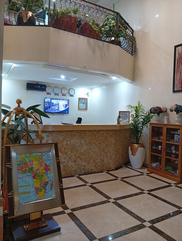 A reception area with a check-in counter, a wall-mounted TV, clocks, a framed map, and a potted plant.