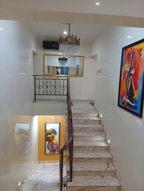 A staircase with marble steps, a chandelier, and artwork on the walls.