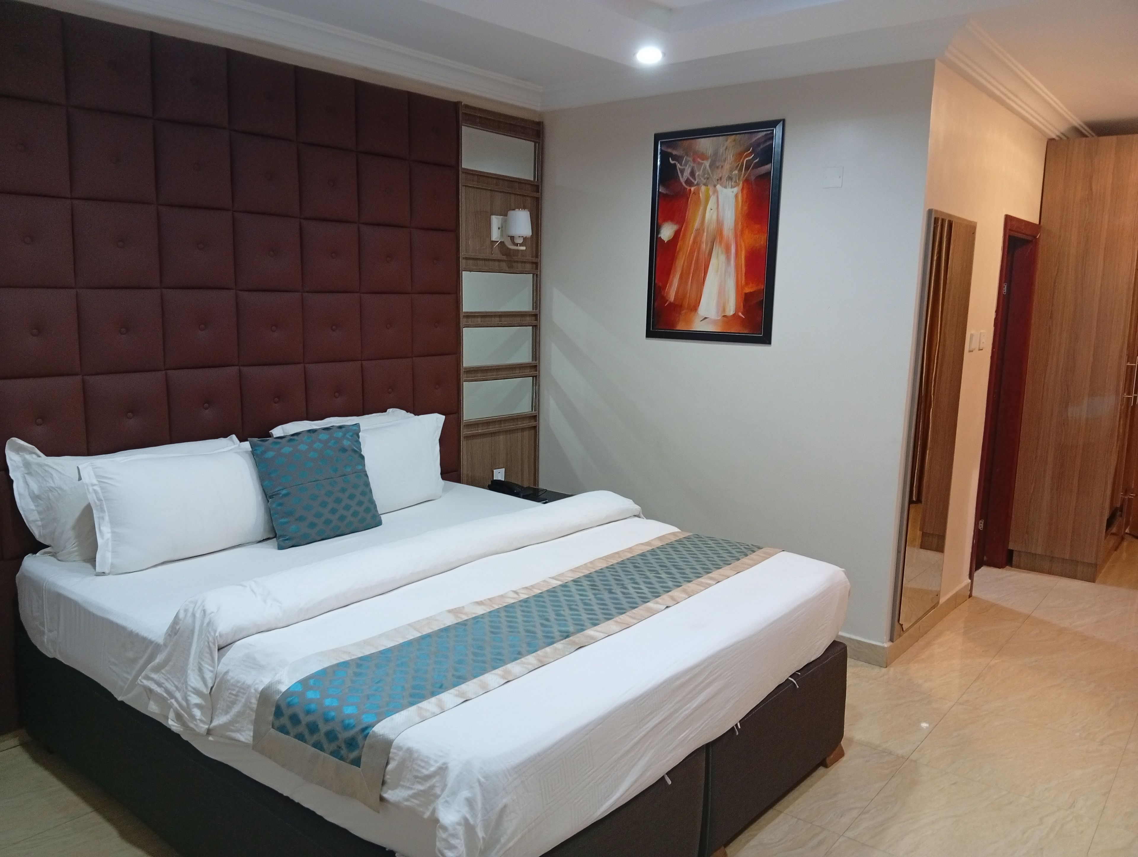A hotel room with a large bed, a headboard with a padded design, a wall-mounted artwork, and a wooden door.