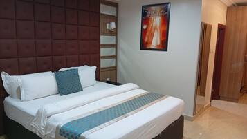 A hotel room with a large bed, a headboard with a padded design, a wall-mounted artwork, and a wooden door.