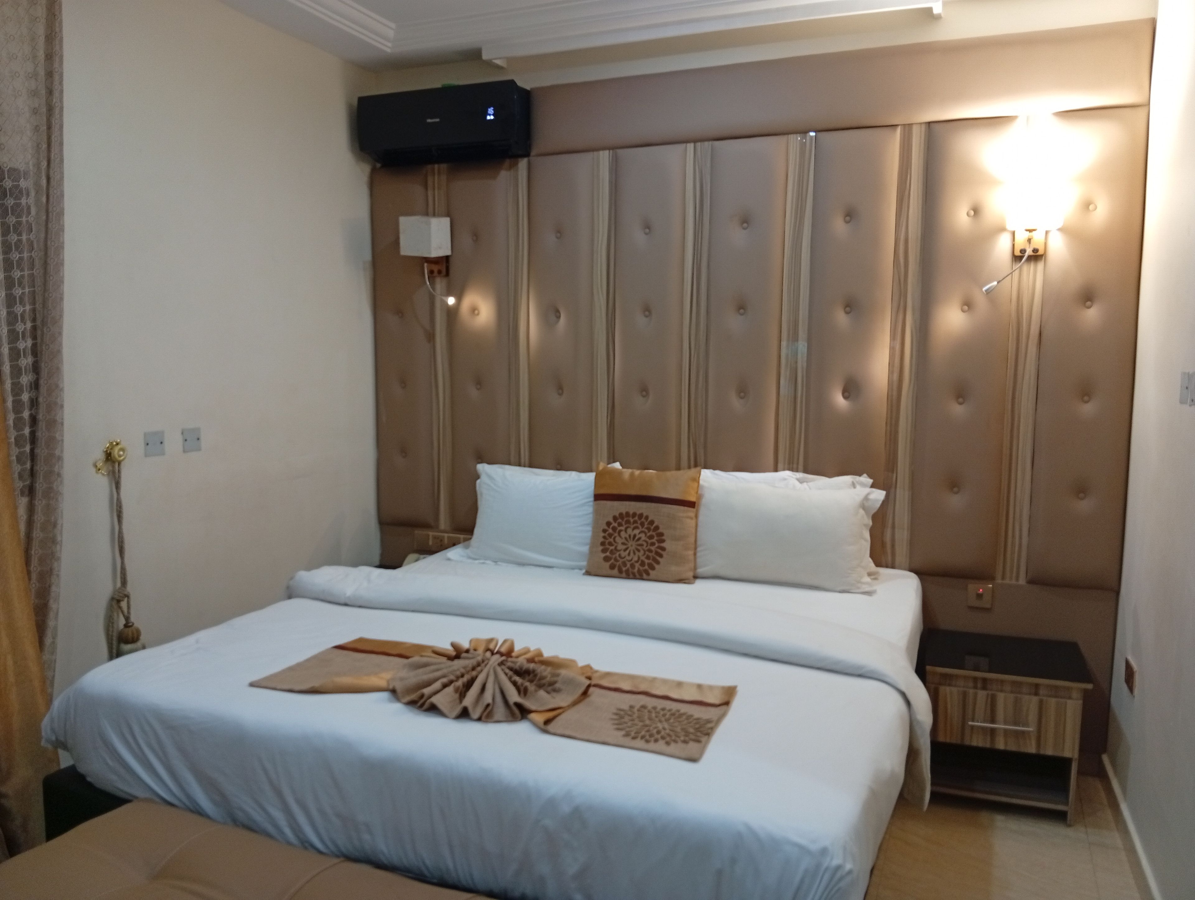 A hotel room with a large bed, a bedside table, a wall-mounted TV, and a wall sconce.