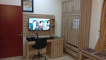 A bedroom with a TV mounted on the wall, a wooden wardrobe, a desk with a chair, and a bed.