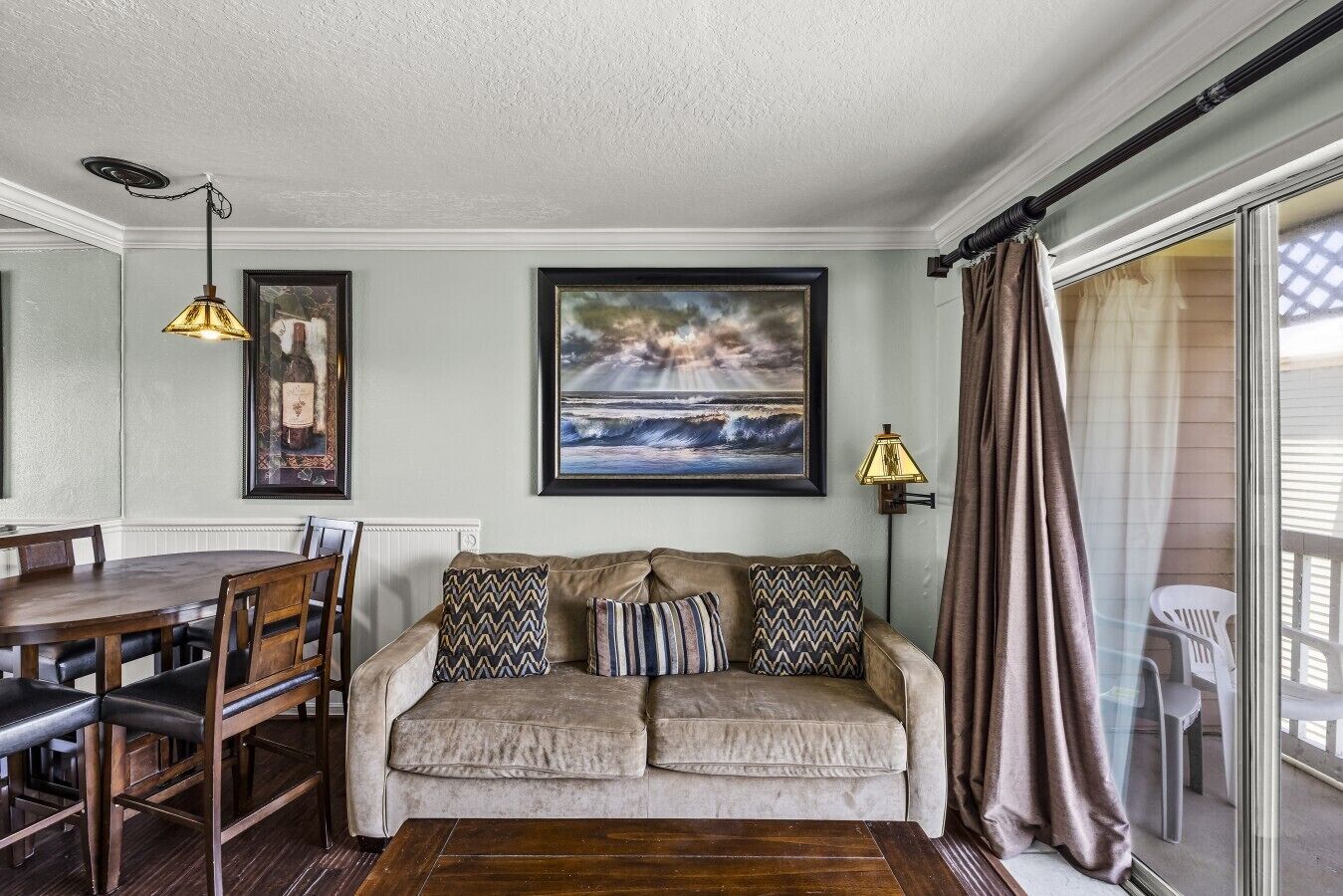 A cozy living area with a sofa, a dining table, and chairs. There are framed pictures on the wall and a lamp on the side.