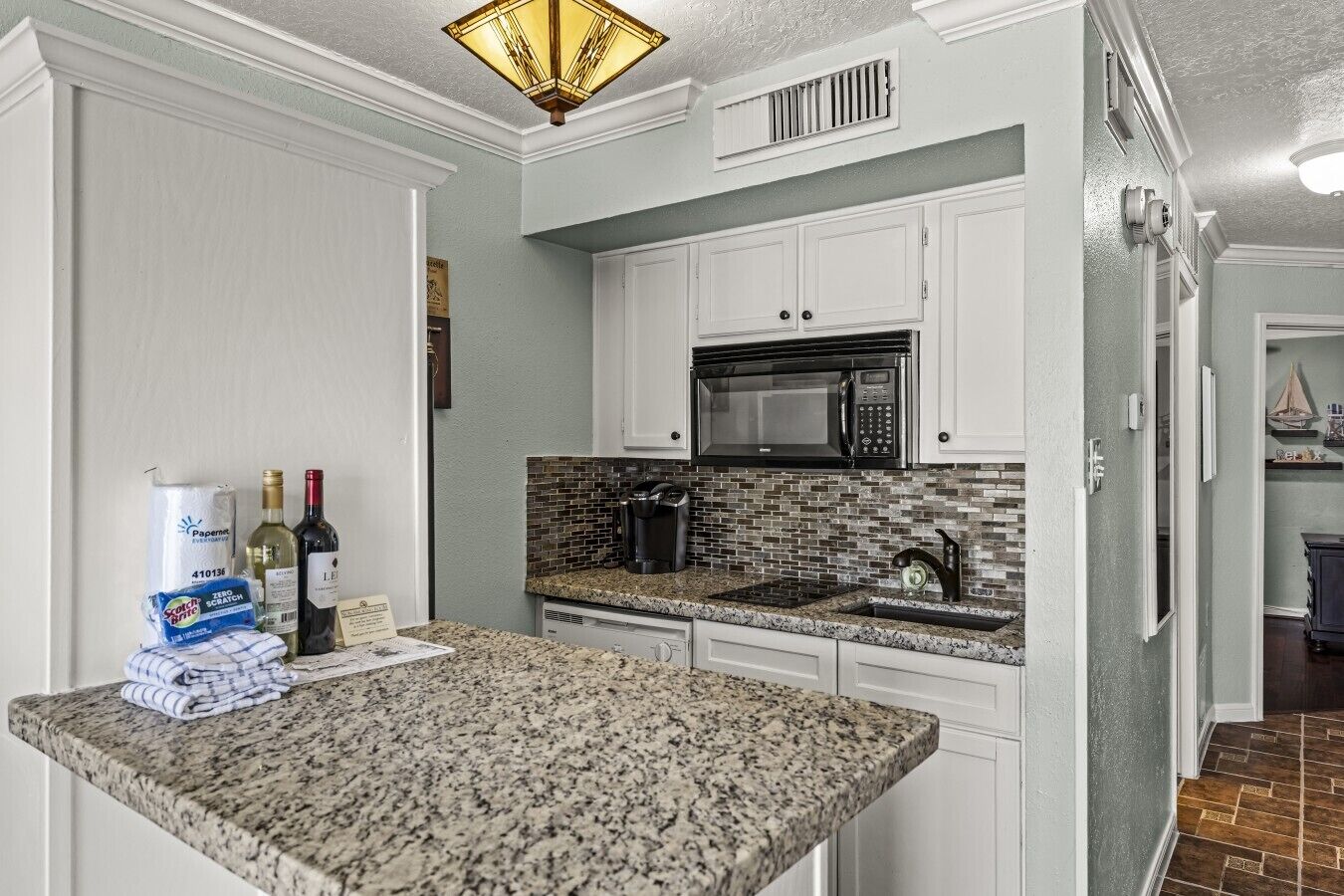 A kitchen with white cabinets, a granite countertop, a microwave, and a coffee maker.