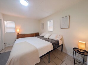 Une chambre à coucher avec un lit, des tables de chevet, une commode et une fenêtre avec des stores.