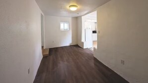 A hallway with wooden flooring, white walls, a small window, and an open door leading to a kitchen area. - Downtown District - Modern Apt Yard, King Bed, W/D (Albuquerque)