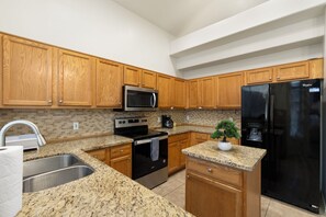 A kitchen with wooden cabinets, a granite countertop, a stainless steel sink, a microwave, an oven, a refrigerator, and a small potted plant. - Spacious 4BR Phoenix Home with Private Pool! (Phoenix)