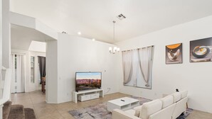 Una sala de estar moderna con televisor de pantalla plana, sofá blanco y una obra de arte en la pared.