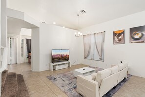 A modern living room with a flat-screen TV, white sofa, and artwork on the wall. - Spacious 4BR Phoenix Home with Private Pool! (Phoenix)