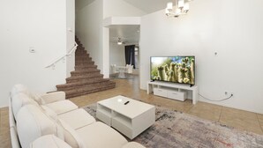 Una sala de estar moderna con una escalera, un televisor de pantalla plana y un sofá blanco.