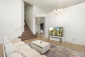 A modern living room with a staircase, a flat-screen TV, and a white sofa. - Spacious 4BR Phoenix Home with Private Pool! (Phoenix)