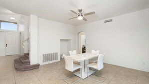 Una habitación amplia con una mesa de comedor, sillas blancas, un ventilador de techo y una escalera.