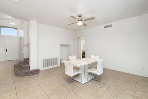 A spacious room with a dining table, white chairs, a ceiling fan, and a staircase. - Spacious 4BR Phoenix Home with Private Pool! (Phoenix)