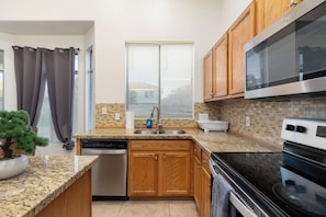 A kitchen with granite countertops, wooden cabinets, a dishwasher, a stove, and a window with blinds. - Spacious 4BR Phoenix Home with Private Pool! (Phoenix)