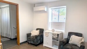 Een kamer met twee gestoffeerde fauteuils, een witte bijzettafel en een raam met jaloezieën.