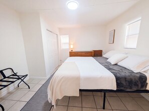 A bedroom with a bed, bedside tables, a chair, a window, and a door. - Downtown District - Modern Apt Yard, King Bed, W/D (Albuquerque)