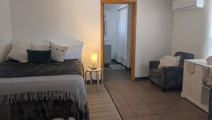Een slaapkamer met een bed, nachtkastje, lamp, stoel, dressoir en een airconditioning.