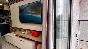 Un salon moderne doté d’un téléviseur à écran plat, d’un meuble en bois et d’une porte-fenêtre coulissante donnant sur un balcon.