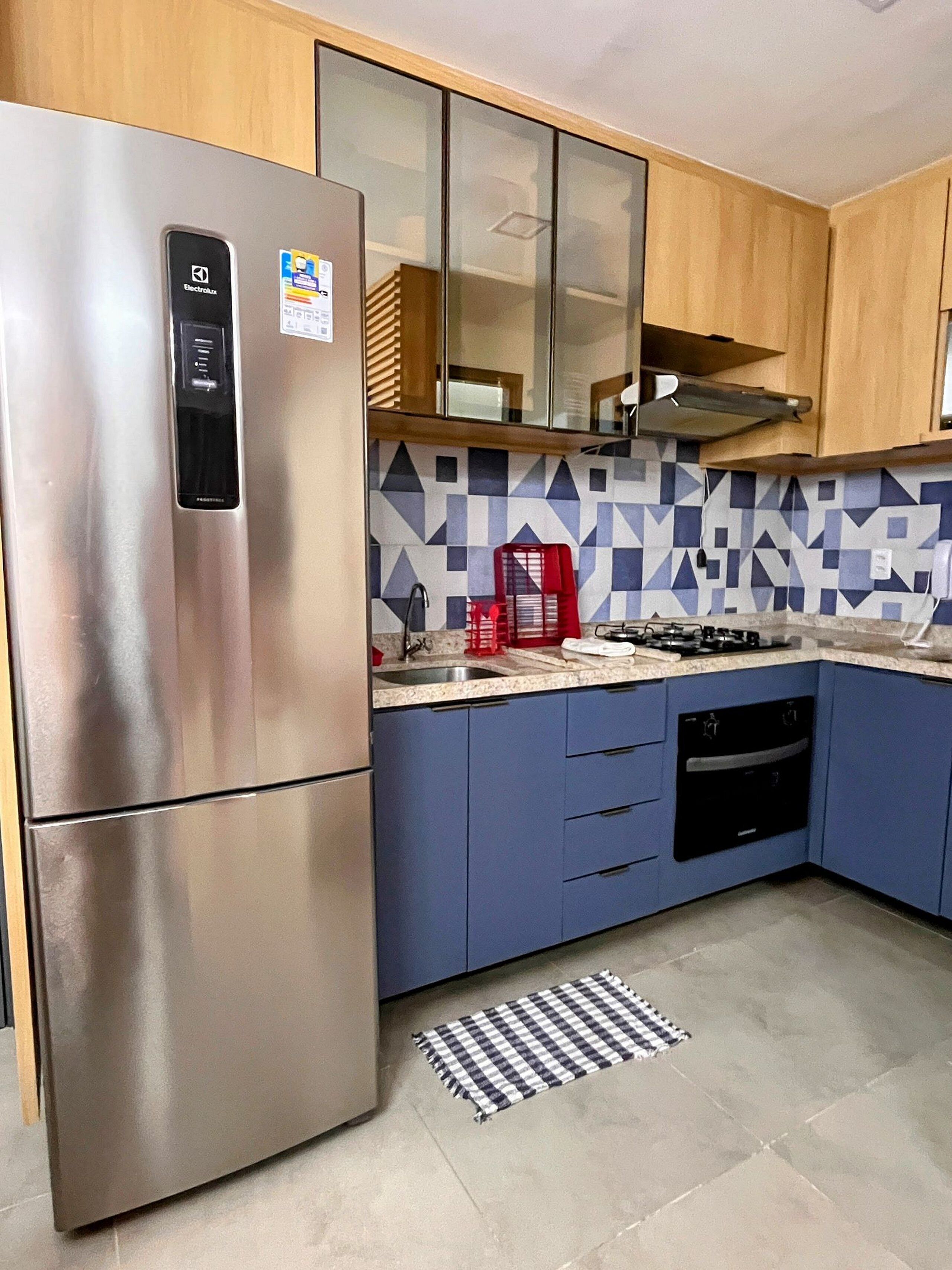Una cocina con refrigerador de acero inoxidable, gabinetes azules, salpicadero con diseño, estufa a gas y lavavajillas.
