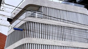 Un bâtiment moderne doté d’une façade à motifs distinctifs, d’une enseigne et de plantes en pot devant l’entrée.