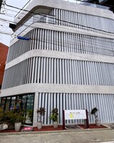 A modern building with a unique ribbed facade, a signboard, and potted plants in front.