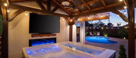 A hot tub with a television above it, a pool, and a covered patio area.
