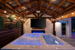 A hot tub with a television above it, wooden beams on the ceiling, and a door to the right. - Casa Arcadia Rejuvenation Retreat (Phoenix)