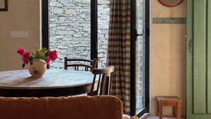 A room with a dining table, chairs, a vase with flowers, a sofa with a floral cushion, a mirror, and a green door.