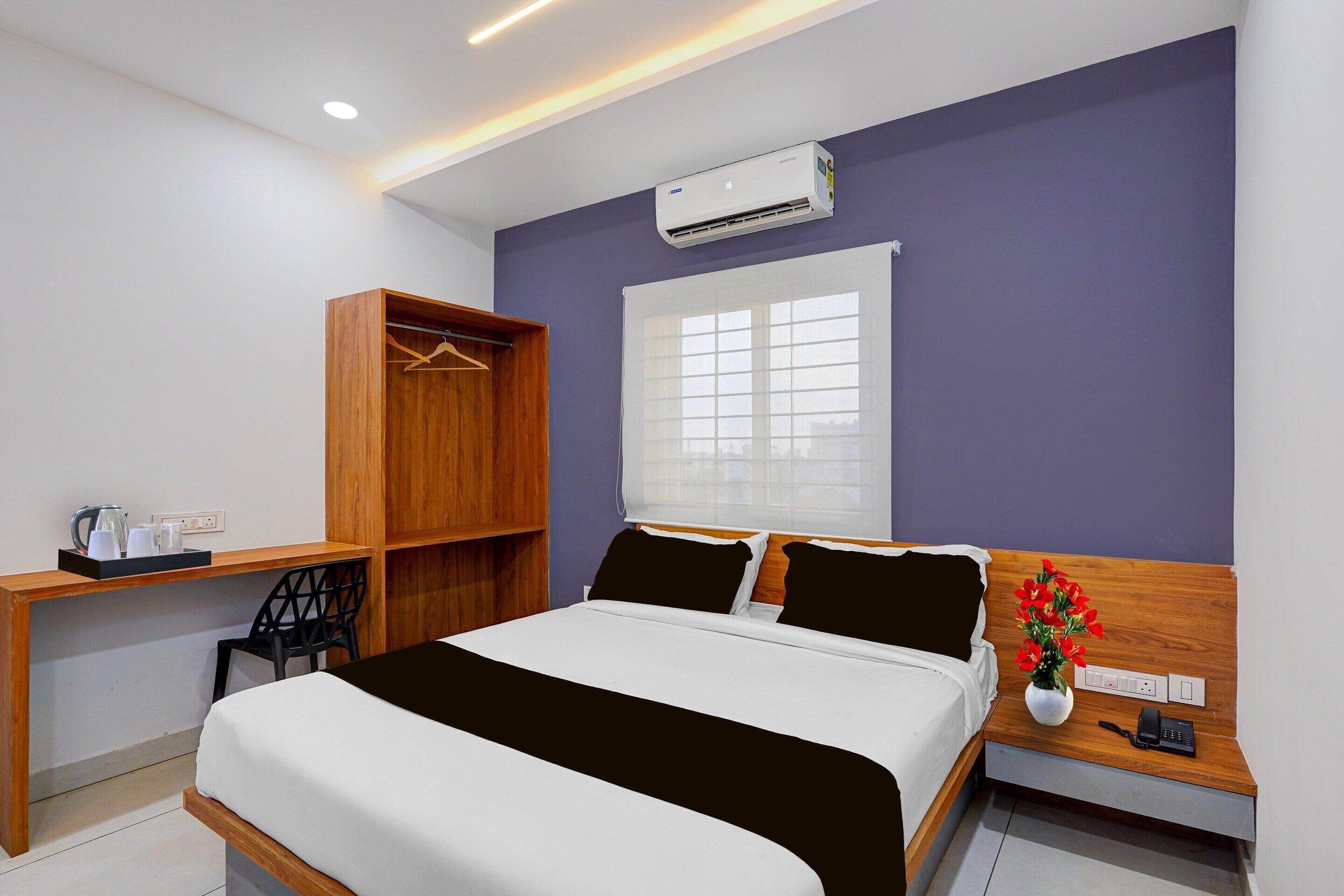 Habitación de hotel con cama, escritorio, armario, ventana con persianas y aire acondicionado.