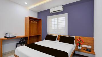 Habitación de hotel con cama, escritorio, armario, ventana con persianas y aire acondicionado.