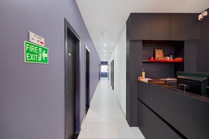 A corridor with a fire exit sign, a reception desk, and a surveillance camera. - Deluxe Brookefield Mall Bangalore (Bengaluru)