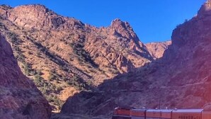A train traveling through a canyon with rocky terrain and a river.