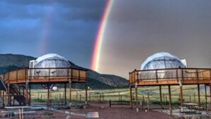 Two dome-shaped structures with wooden frameworks, set in an open area with a mountain in the background.