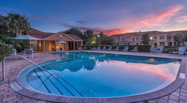 Une piscine avec un espace de détente, un coin salon abrité et un bâtiment en arrière-plan.