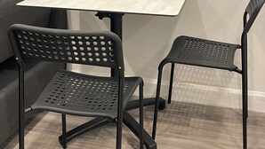 Ett litet, modernt rum med en grå soffa, ett vitt bord och två svarta stolar med perforerad rygg.