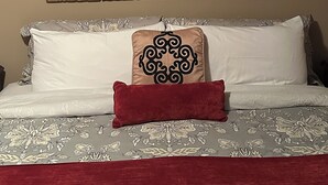 Ein Bett mit gemusterten Betttextilien, einem dekorativen Kopfteil und zwei gerahmten Wandbildern darüber.