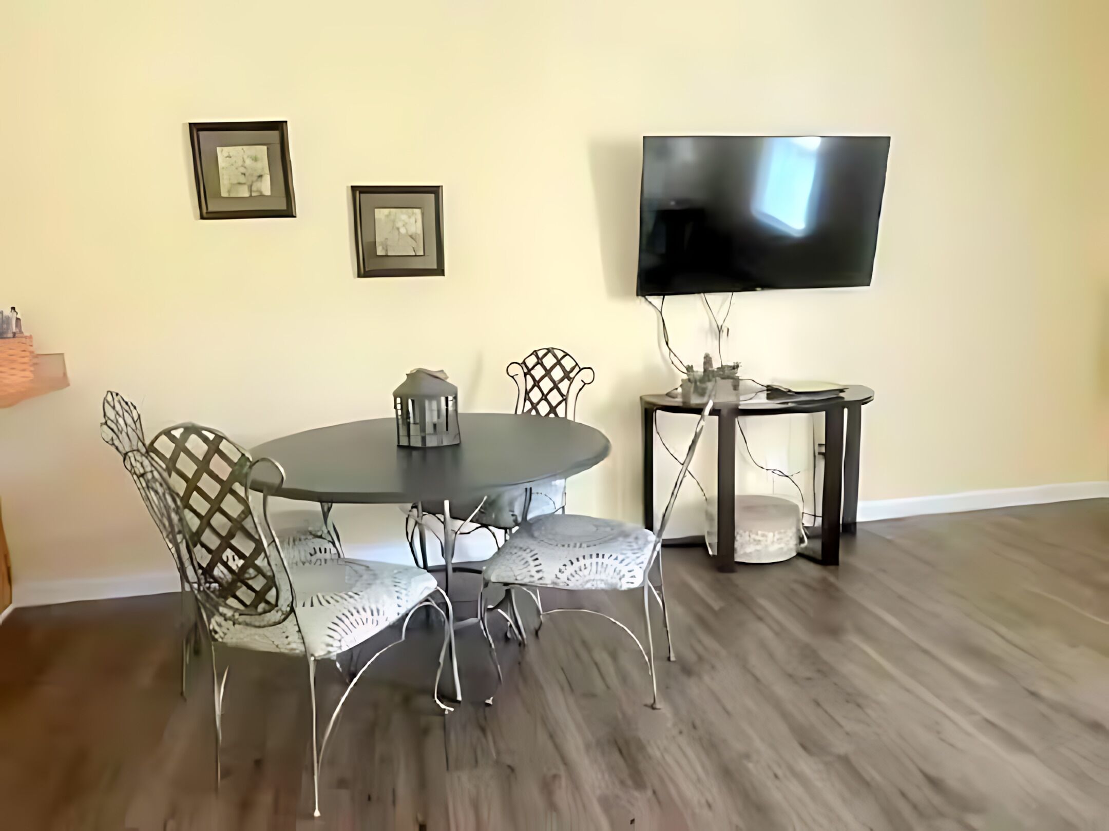 A dining area with a round table, four chairs, a television, and two framed pictures on the wall.