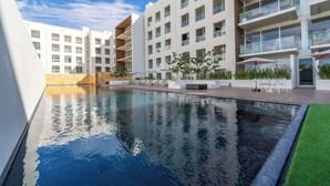 Een modern hotel met een zwembad, meerdere balkons en buitenzitplaatsen.